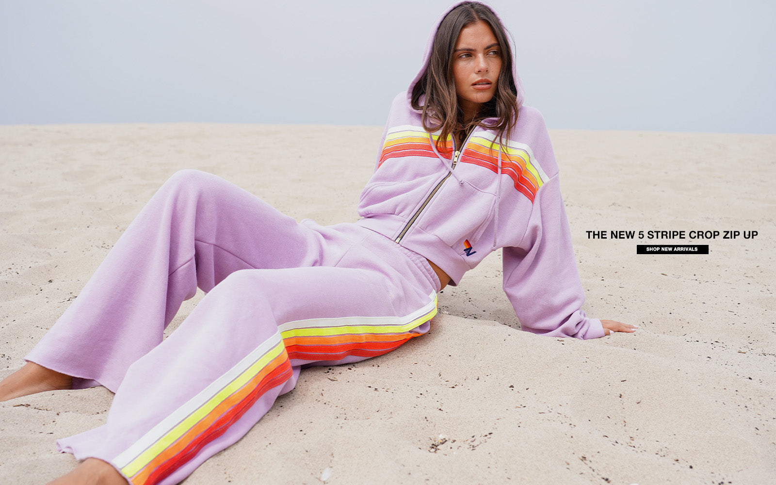 Person wearing a lavender tracksuit with rainbow stripes on a beach