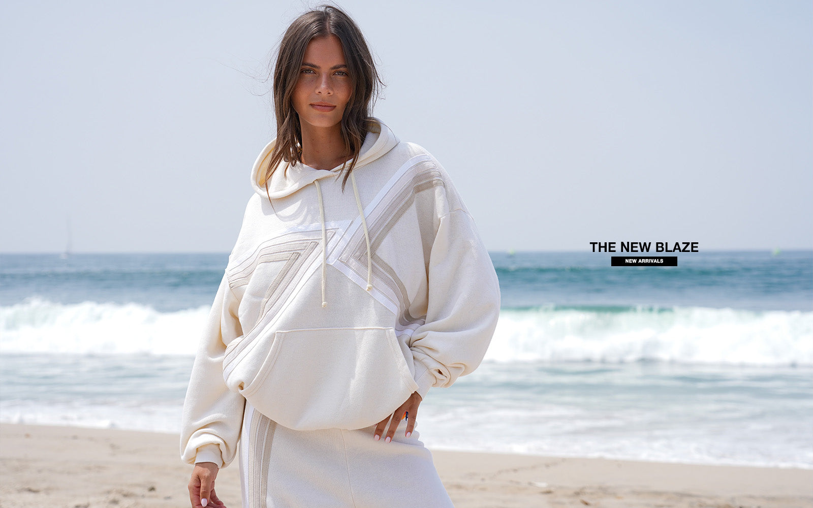 Woman in a white outfit standing on a beach with ocean waves in the background