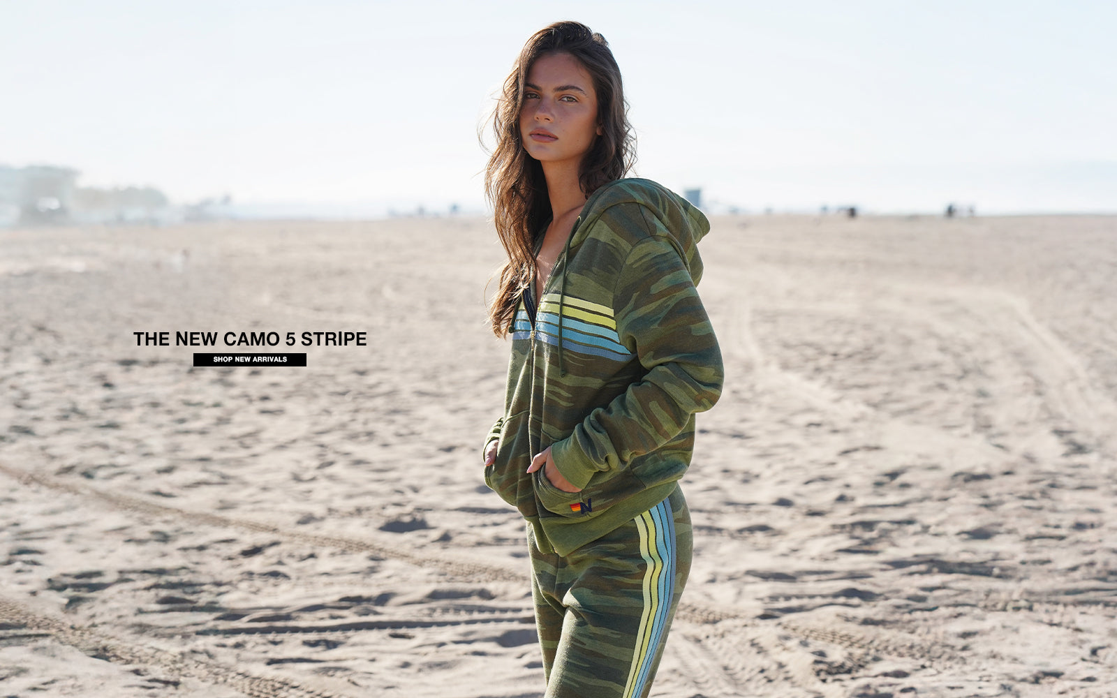 Woman wearing a green tracksuit with 'Camo 5 Stripe' text overlay in a desert setting