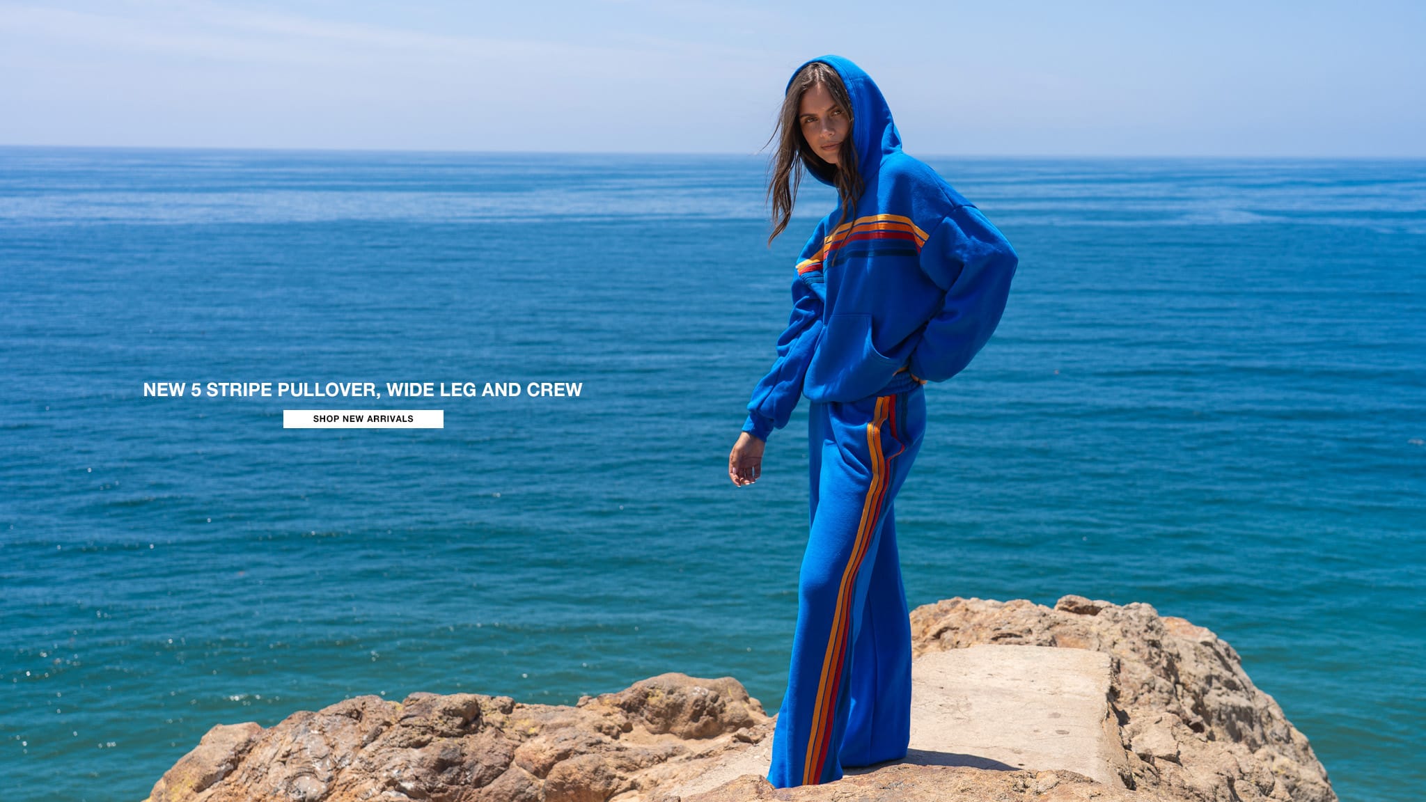 Person wearing a blue outfit with a stripe on a rocky outcrop by the ocean