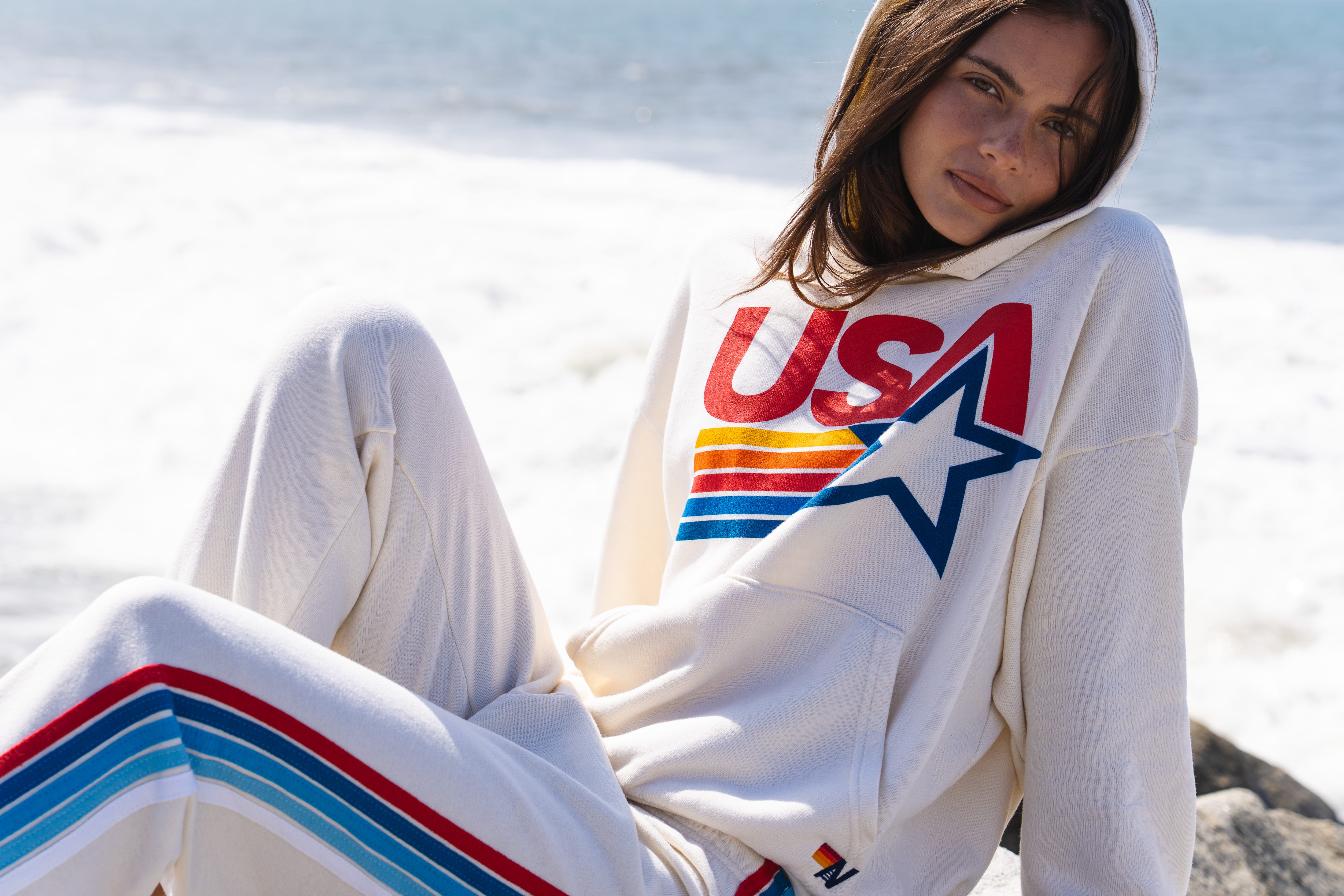Person wearing a white sweatshirt with 'USA' logo sitting on a beach.