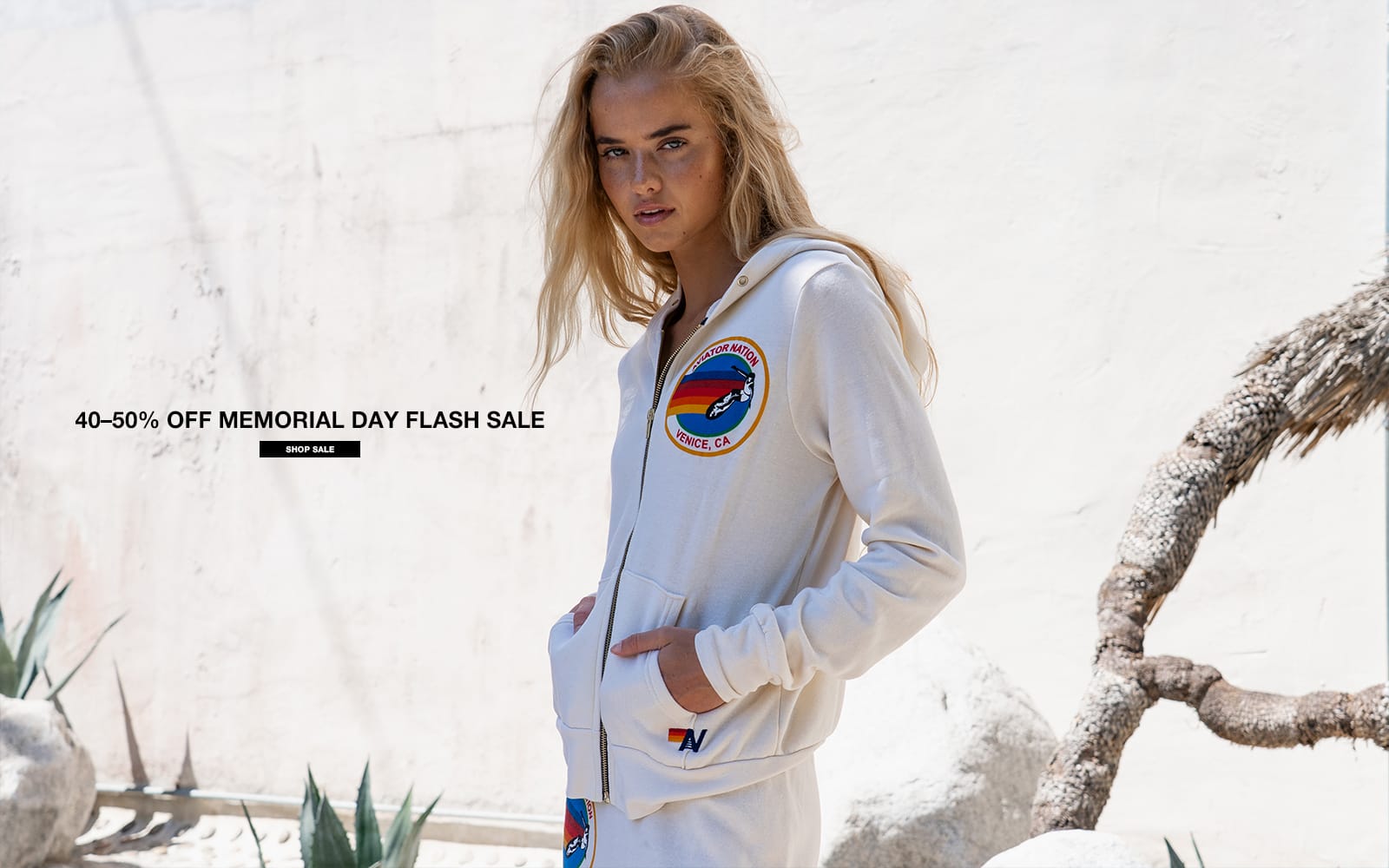 Woman wearing a white hoodie with a logo, standing against a desert background with promotional text overlay.