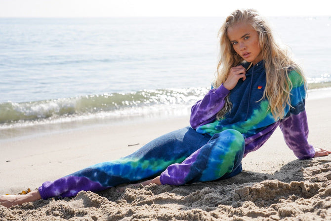 Person wearing a tie-dye outfit sitting on the beach.